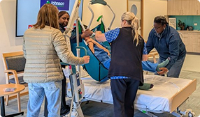 Hospital-setting with nurses showing students how to handle a patient in a medical bed.